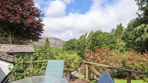 A glass-top table with two chairs, a wooden deck, and a view of a mountainous landscape. - The Farmhouse (Coniston)