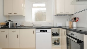 A modern kitchen with white cabinets, a dishwasher, an oven, and a window providing natural light. - Alway (Lifton)