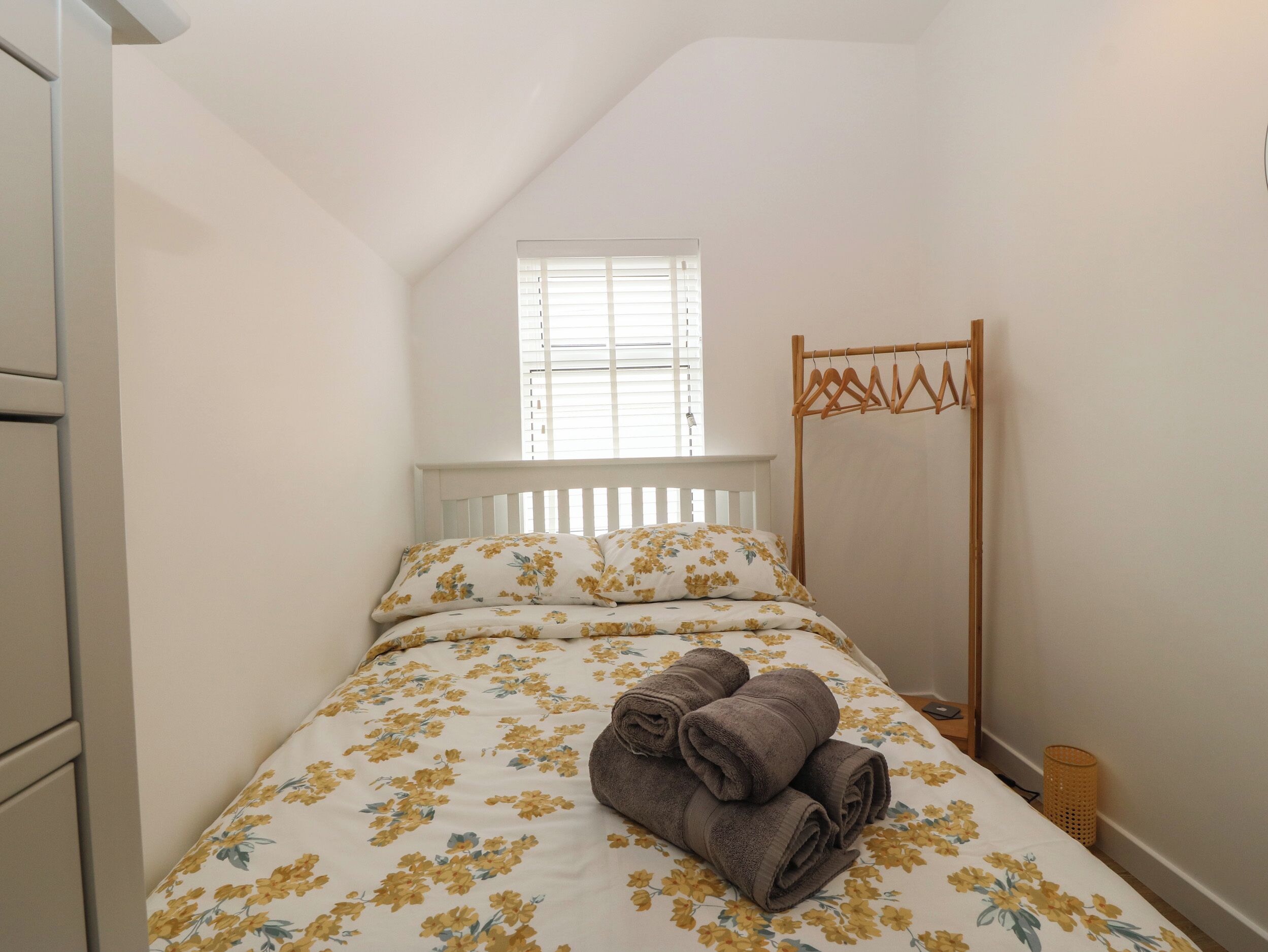 Une chambre avec un lit, une fenêtre, un étendoir en bois et un petit panier en osier.