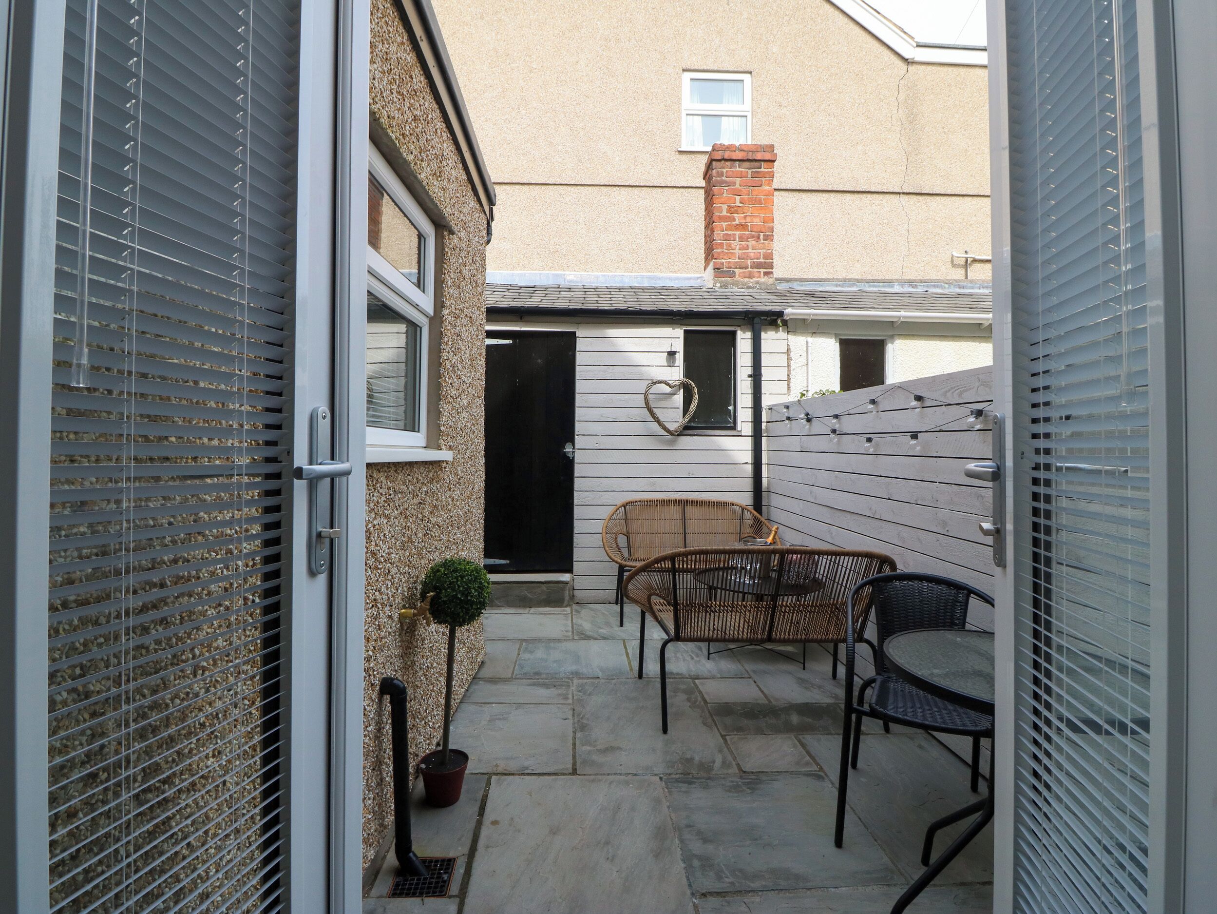 A narrow patio with a table and chairs, a potted plant, and a black door.