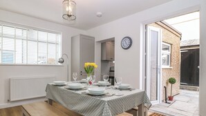 A dining area with a table set for four, a clock on the wall, and a view of the outside. - Elsinore (Conwy)