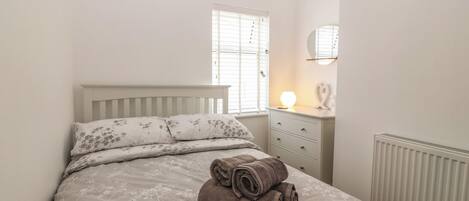 A bedroom with a bed, a bedside table with a lamp, and a radiator.