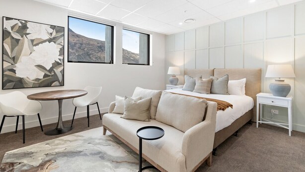 Un dormitorio moderno con una cama grande, un sofá, una mesita y dos ventanas con vistas a la montaña.