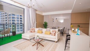 A modern living room with a glass coffee table, a sofa with patterned cushions, a dining area with a white table, and a kitchen counter. - Executive 1 Br -Gtc with gym & Pool (Nairobi)