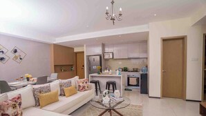 A modern living room with a sofa, coffee table, and kitchen in the background. - Executive 1 Br -Gtc with gym & Pool (Nairobi)