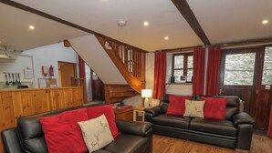 A cozy living room with two black leather sofas, red cushions, and a wooden floor.