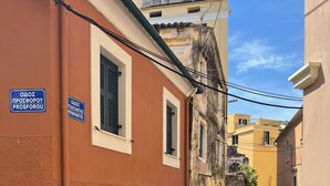 A narrow street with cobblestone pavement, buildings with traditional architecture, and a sign indicating a location. - Casa Di Porto (Kerkira)