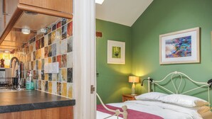 A bedroom with a bed, a nightstand, a lamp, and a green wall with two framed pictures. - The Barn (Lifton)