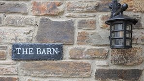 A stone wall with a sign reading "THE BARN" and a lantern attached to it. - The Barn (Lifton)