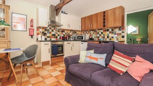 A cozy kitchen with wooden cabinets, a tiled backsplash, and a purple sofa with cushions. - The Barn (Lifton)