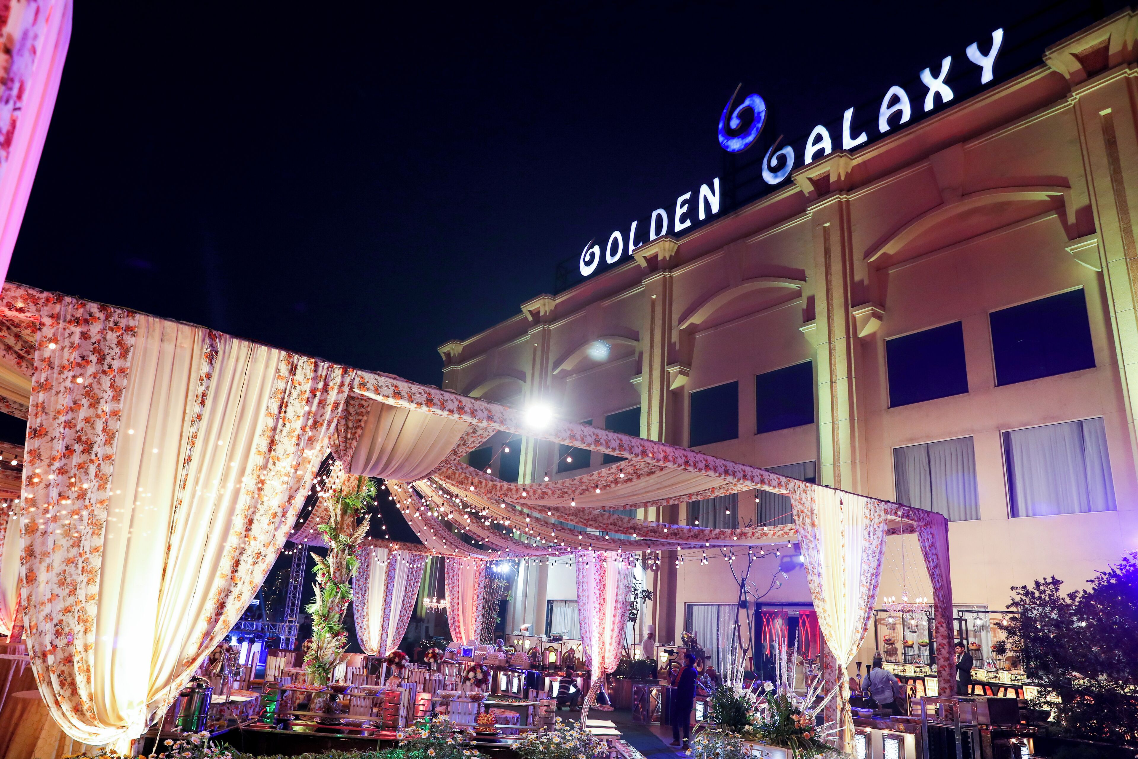 A hotel named "Golden Galaxy" with a covered outdoor area decorated with drapes and lights.