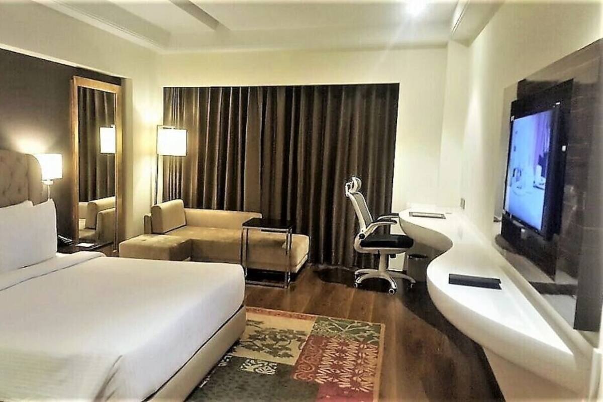 Quarto de hotel com uma cama grande, sofá, escrivaninha, televisão e banheiro.