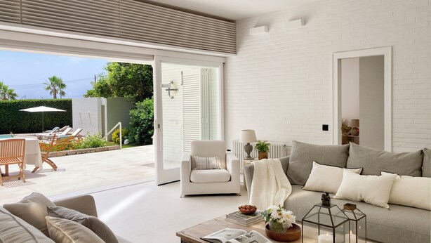 A modern living room with a sofa, coffee table, and a view of an outdoor pool area. - Villa with swimming pool in front of the sea (Roda de Berà)