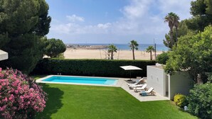 A swimming pool with lounge chairs, a view of the beach, and a clear sky. - Villa with swimming pool in front of the sea (Roda de Berà)