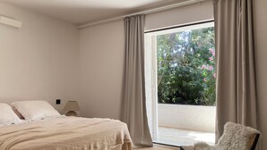 A bedroom with a bed, a chair, and a view of greenery outside. - Villa with swimming pool in front of the sea (Roda de Berà)