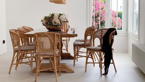 A dining area with wicker chairs, a wooden table, and a hanging light fixture. - Villa with swimming pool in front of the sea (Roda de Berà)