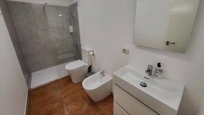 Et moderne badeværelse med bruser, toilet, bidet og en vask med spejl.