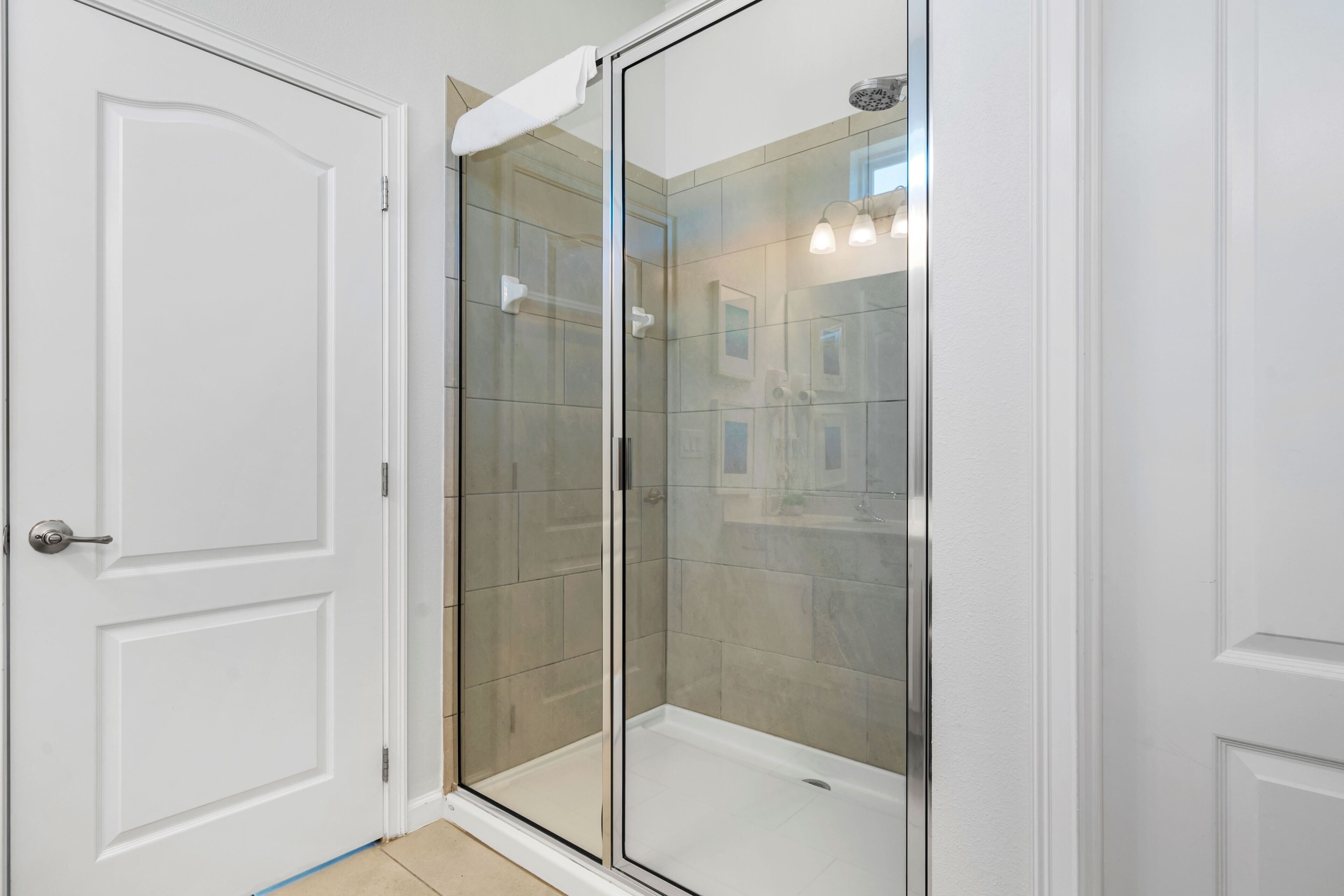 A modern bathroom with a glass shower enclosure, white tiled walls, and a white door.