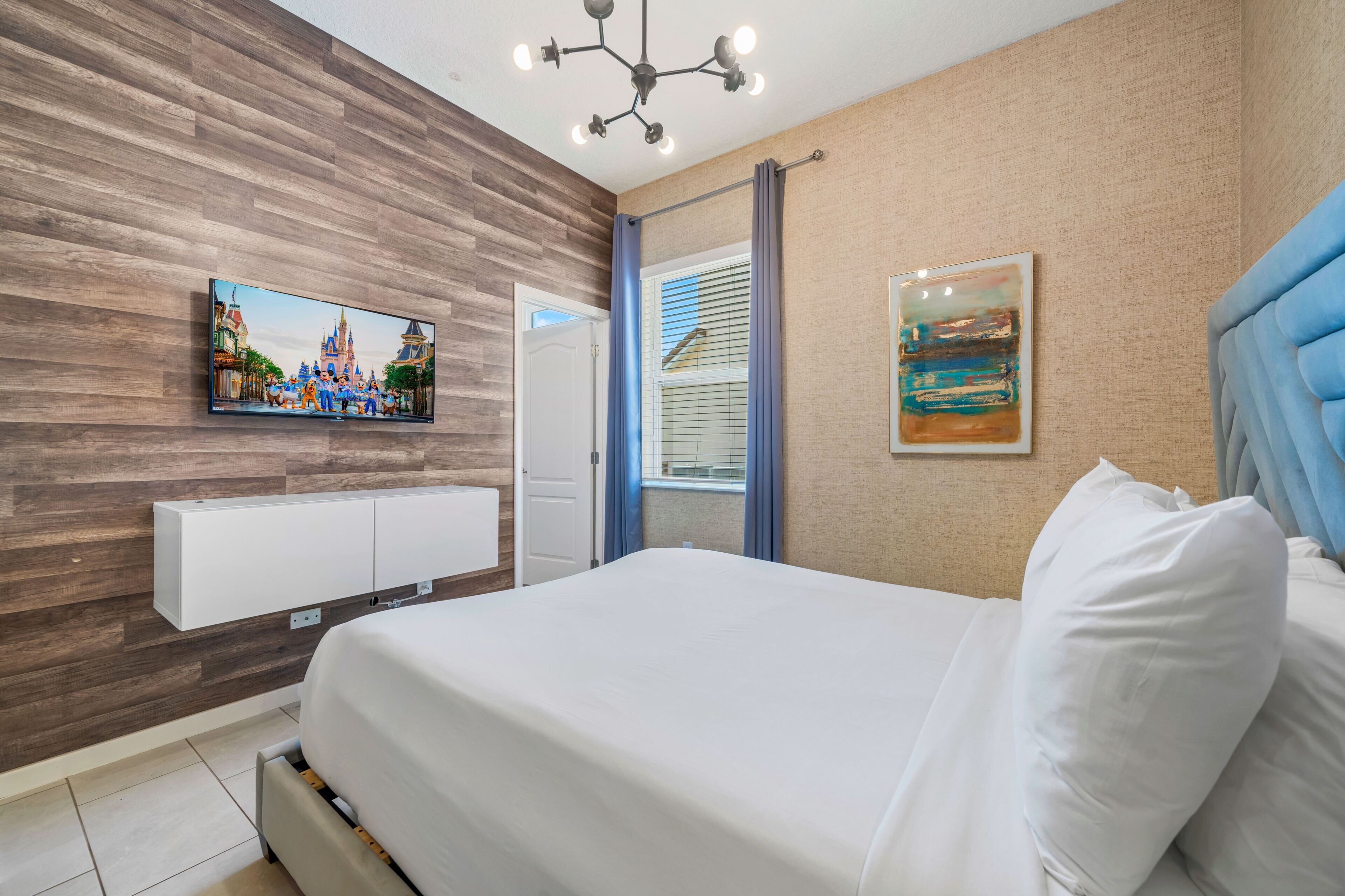Et moderne hotelværelse med en trævæg, et fladskærms-tv, en seng med hvide sengetøj og en blå sengegavl, samt et billede.