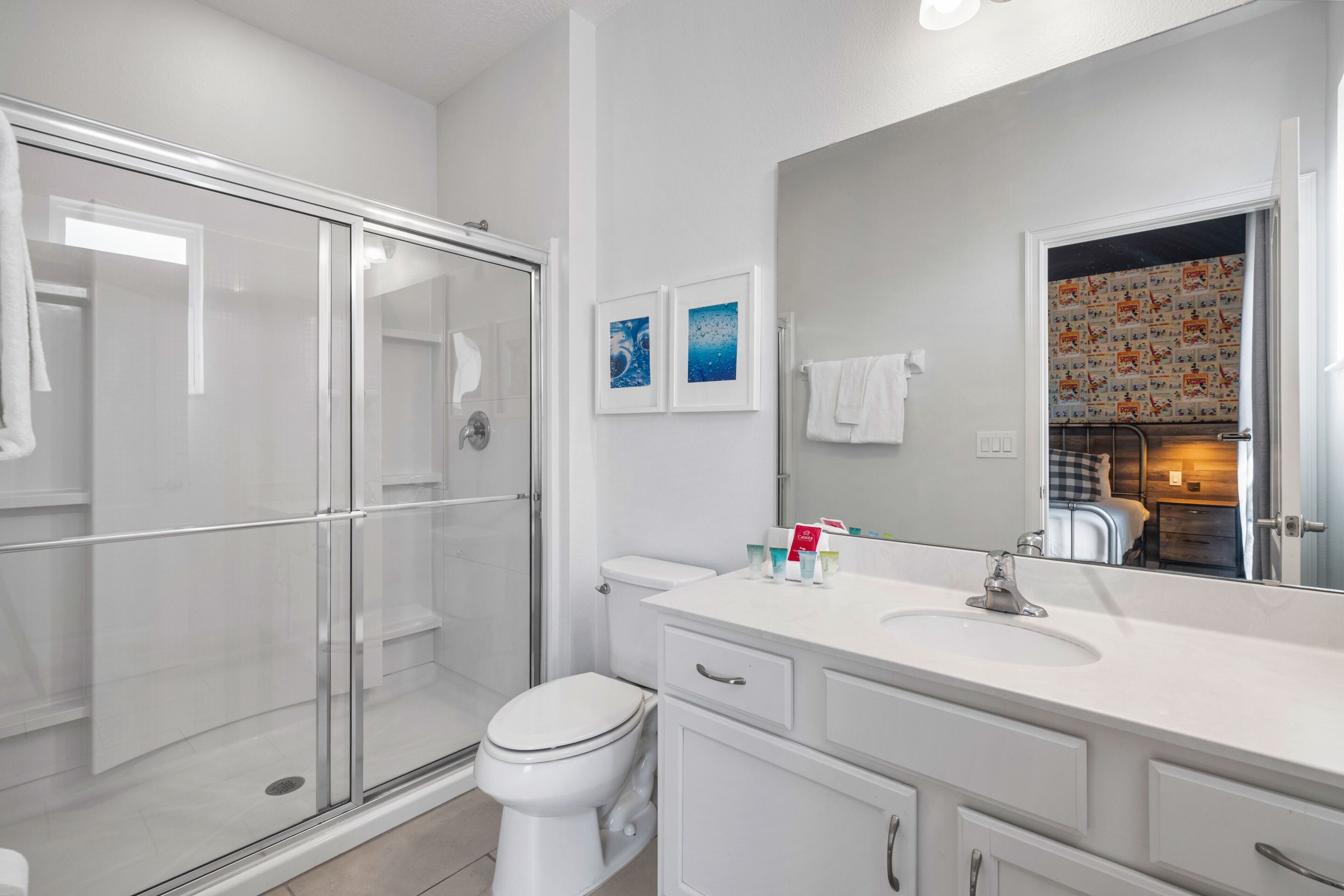 Un baño moderno con cabina de ducha de vidrio, inodoro, lavabo con espejo y toallero.