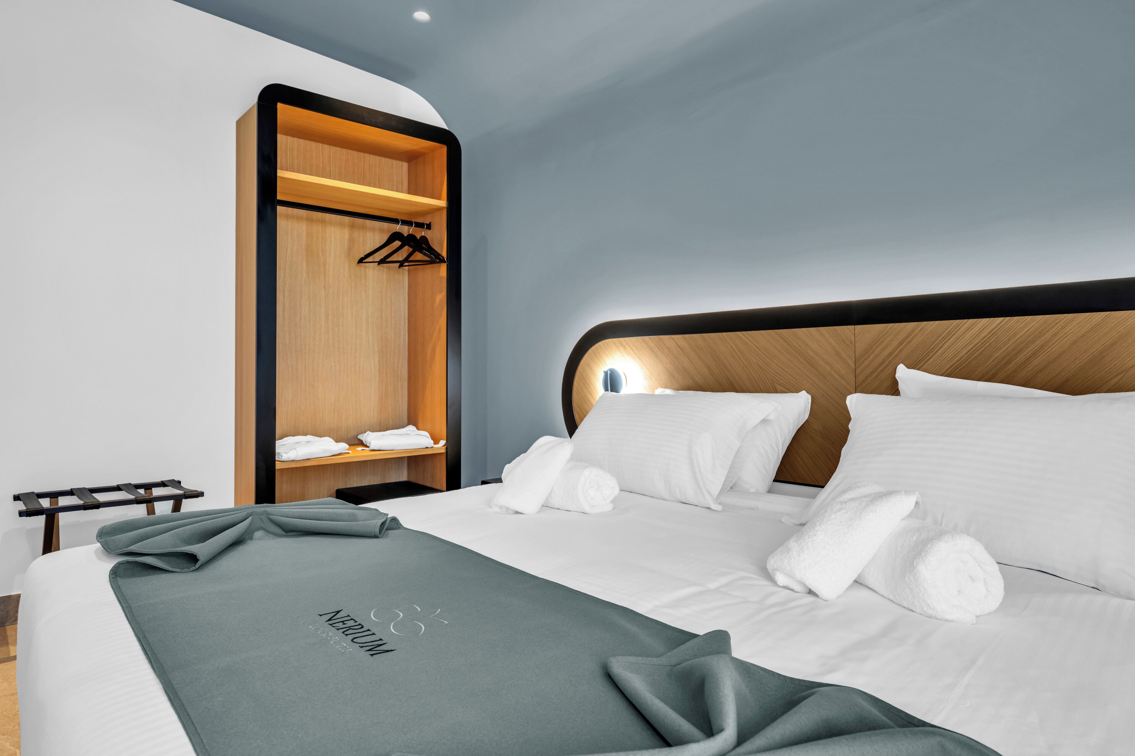 A modern hotel room with a neatly made bed, a built-in wardrobe, and a bedside table with a lamp.