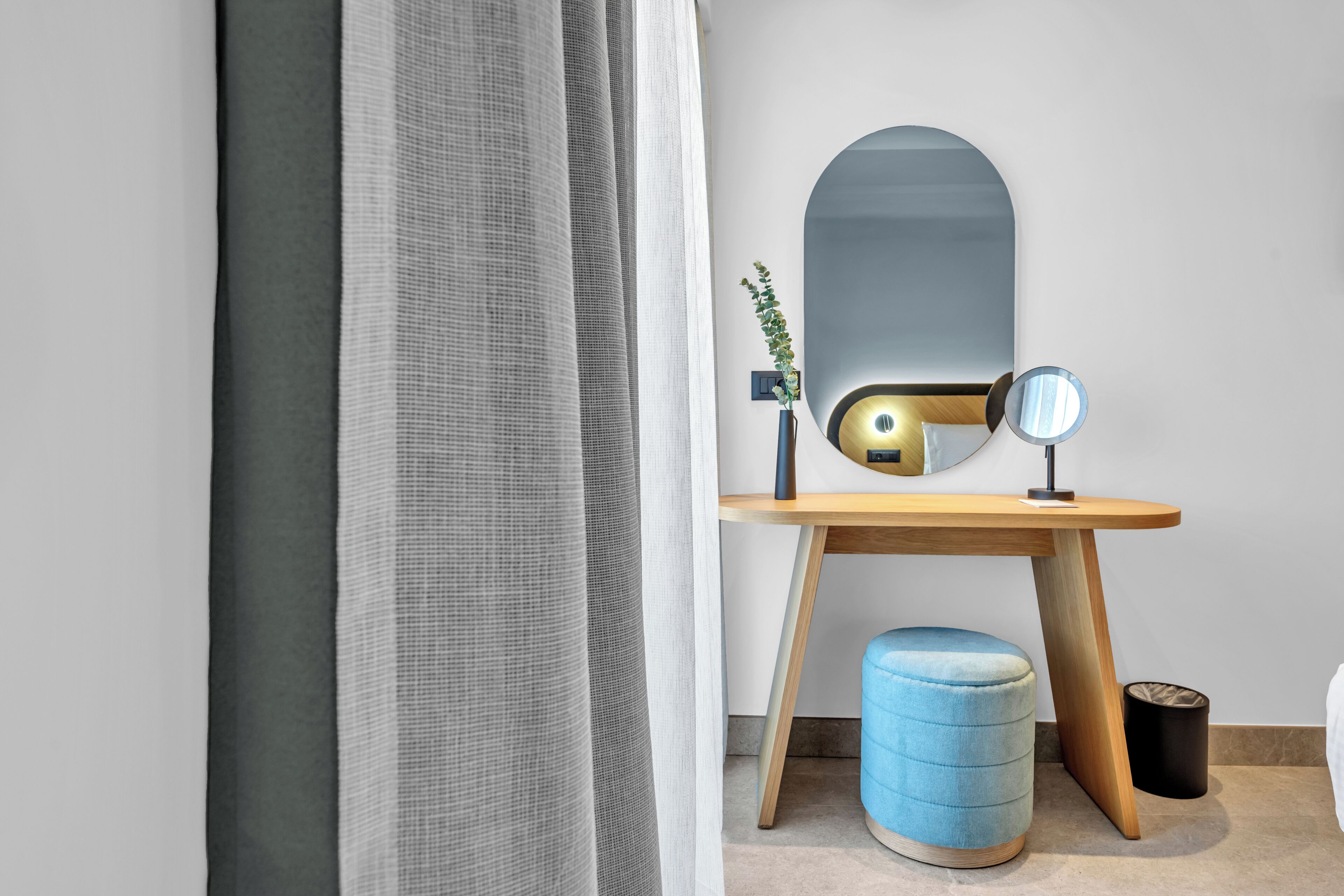 A bathroom with a wooden vanity, a round mirror, a blue stool, and a small plant.