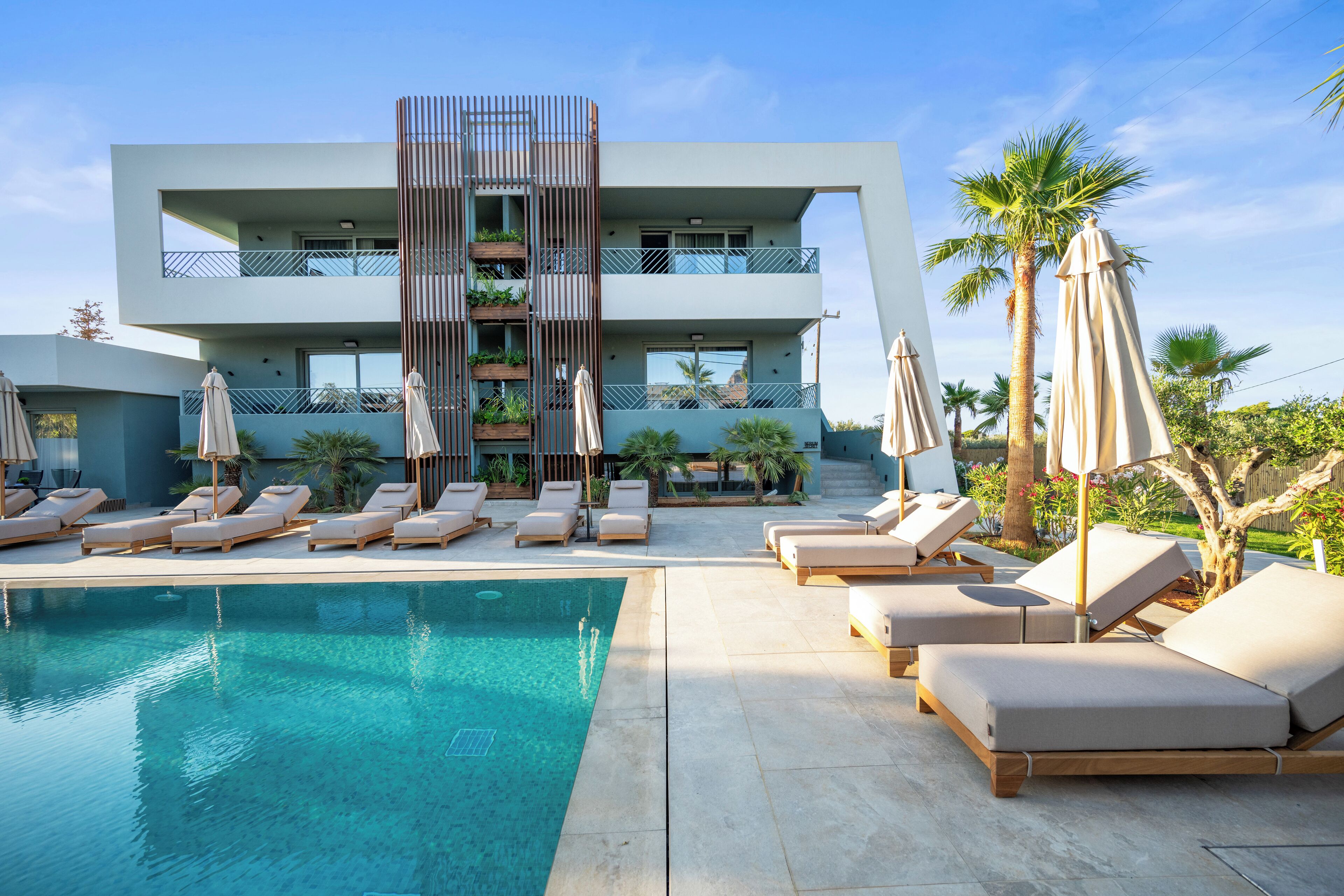 A modern hotel with a pool, lounge chairs, and palm trees.