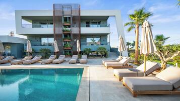 A modern hotel with a pool, lounge chairs, and palm trees.