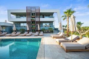 Un hotel moderno con piscina, sillones de descanso y palmeras.
