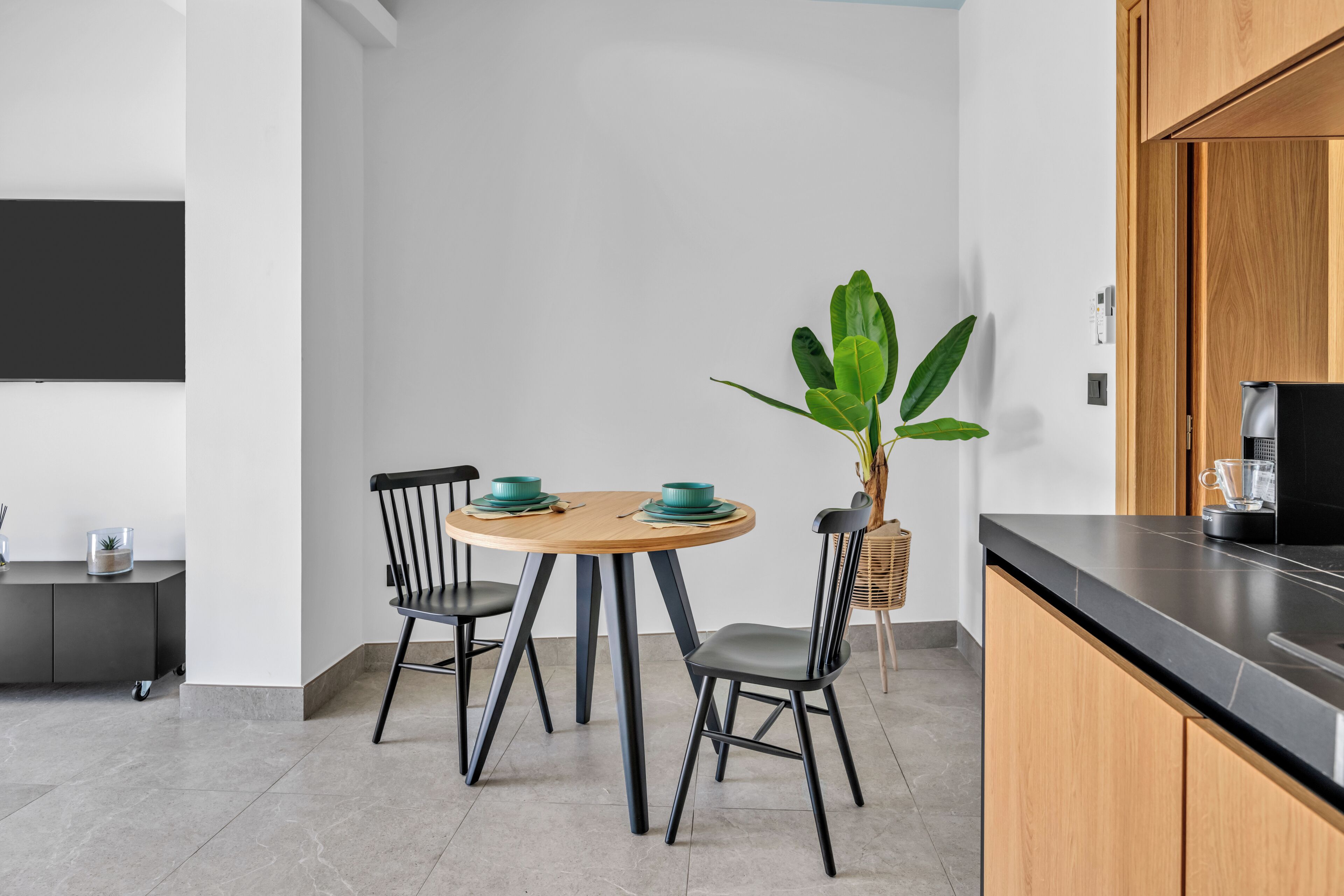 A modern kitchen with a round wooden table, two black chairs, and a potted plant.