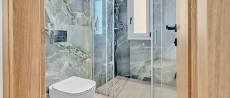 Un baño moderno con pared de mármol, ducha con cerramiento de vidrio y un inodoro blanco.