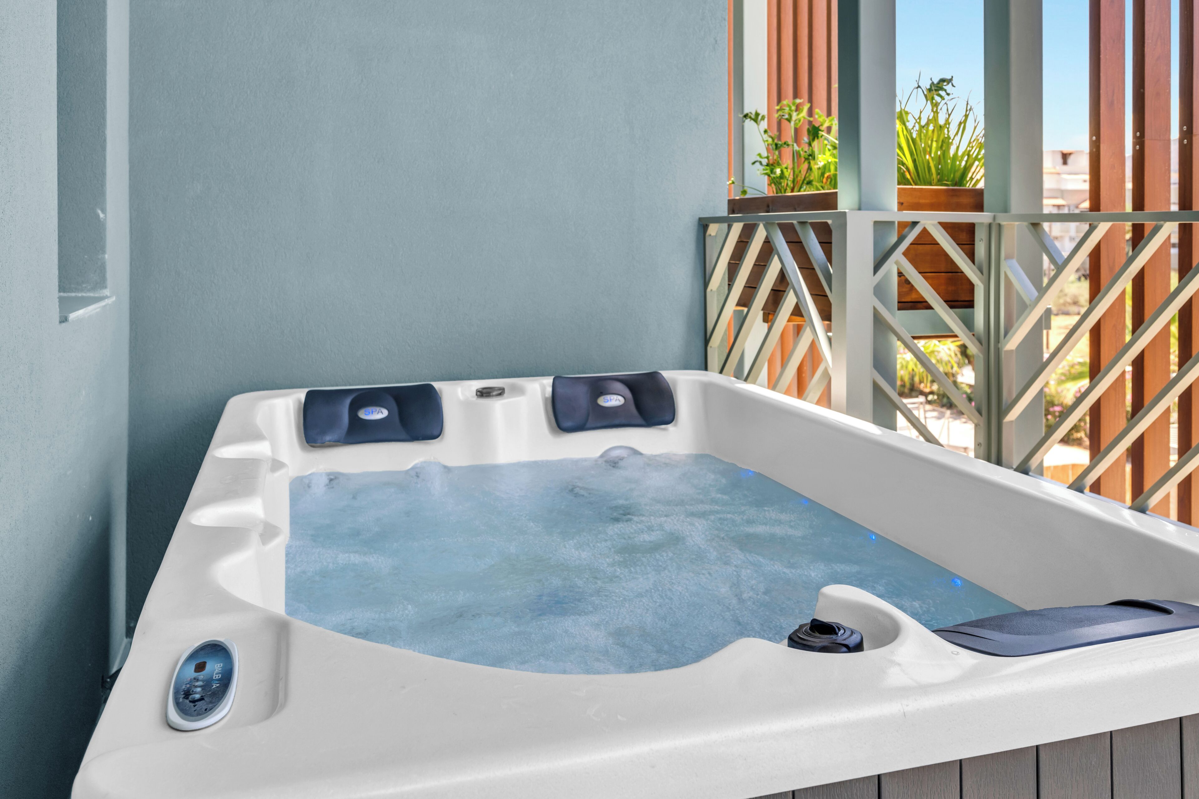 A hot tub with a control panel, surrounded by a wooden deck and a metal railing.