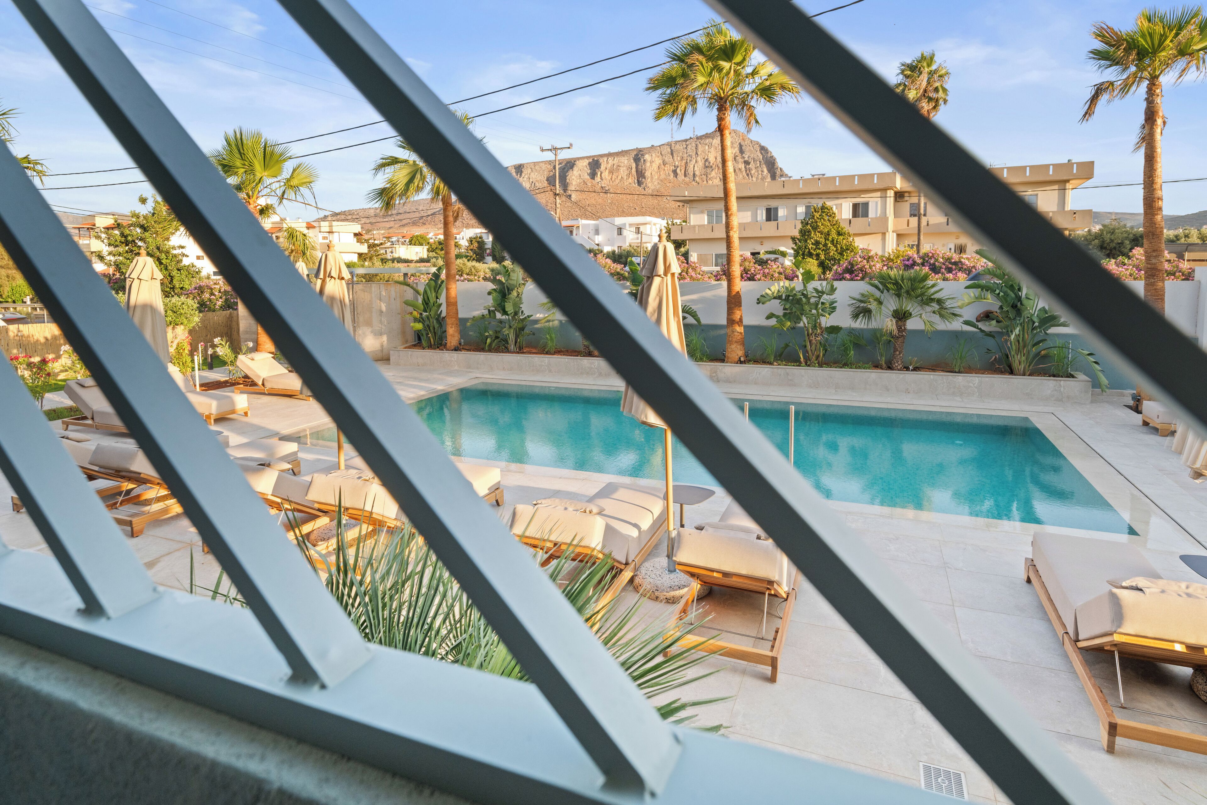 A pool area with lounge chairs and umbrellas, surrounded by palm trees and a building in the background.
