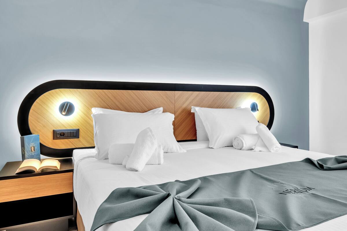 A modern hotel room with a wooden headboard, white bedding, and a neatly made bed with a green throw blanket.