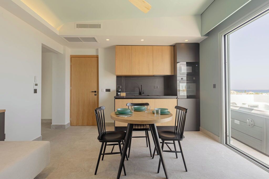 A modern kitchen with wooden cabinets, a dining table with chairs, and a view through a large window.