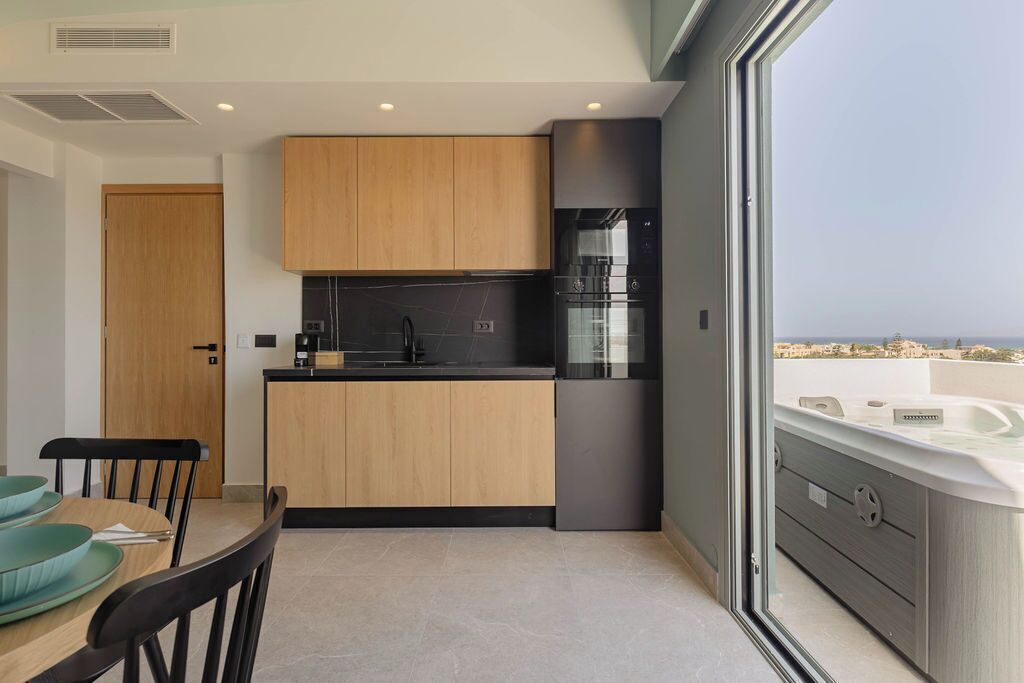 A modern kitchen with a wooden island, black appliances, and a view of the sea through a large window.
