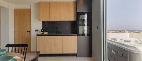 A modern kitchen with a wooden island, black appliances, and a view of the sea through a large window.