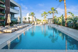 Una piscina con sillones de descanso y palmeras.