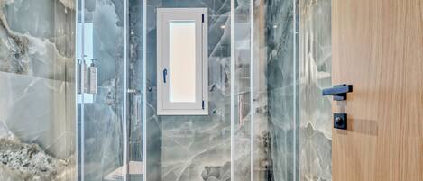 A modern bathroom with a glass-enclosed shower, marble walls, and a wooden door.