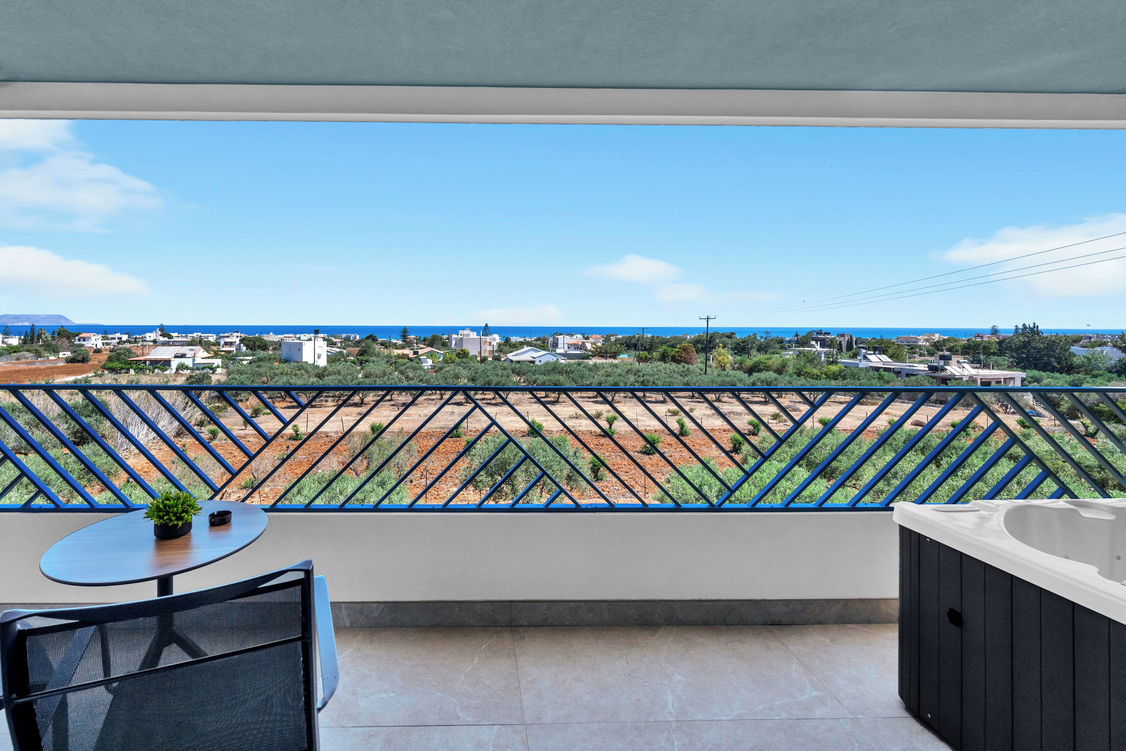 Ein Balkon mit Blick auf eine Küstenstadt, ein kleiner Tisch mit einer Pflanze und eine Whirlwanne.