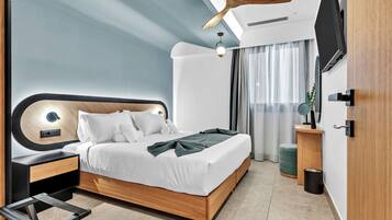A modern bedroom with a wooden bed, a ceiling fan, a bedside table, a TV mounted on the wall, and a window with curtains.