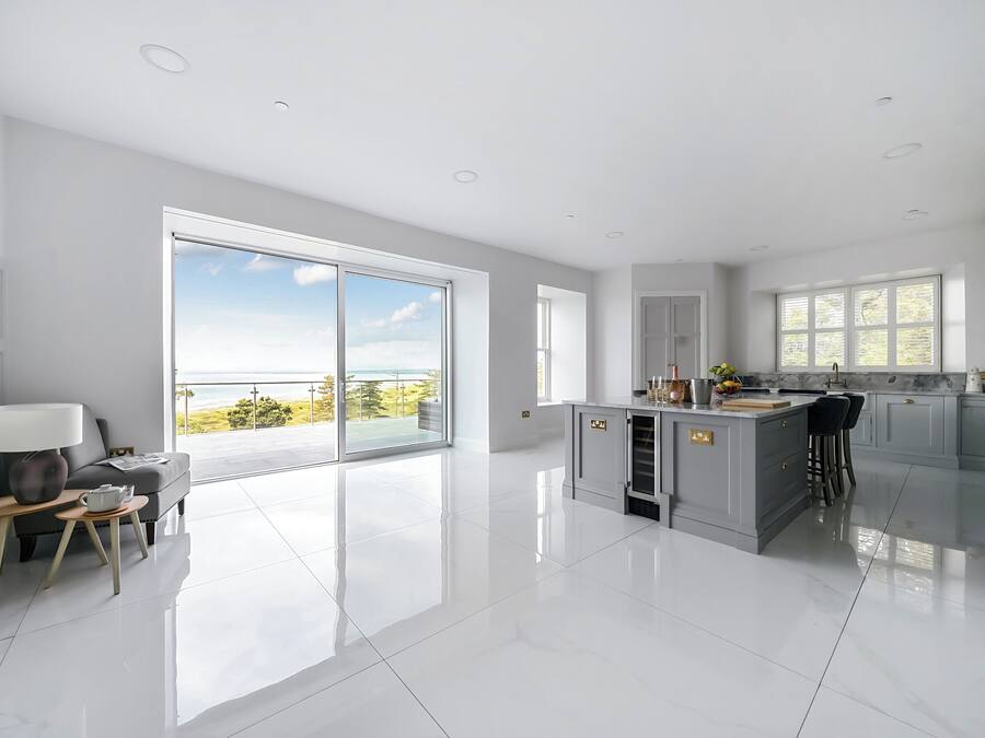 Una cocina moderna con una isla grande, un comedor con mesa y sillas, y un balcón con vista al mar.