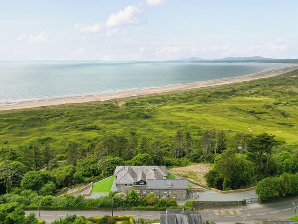 A coastal property with a stone building, a grassy lawn, and a view of the sea. - Plas Amherst (Harlech)