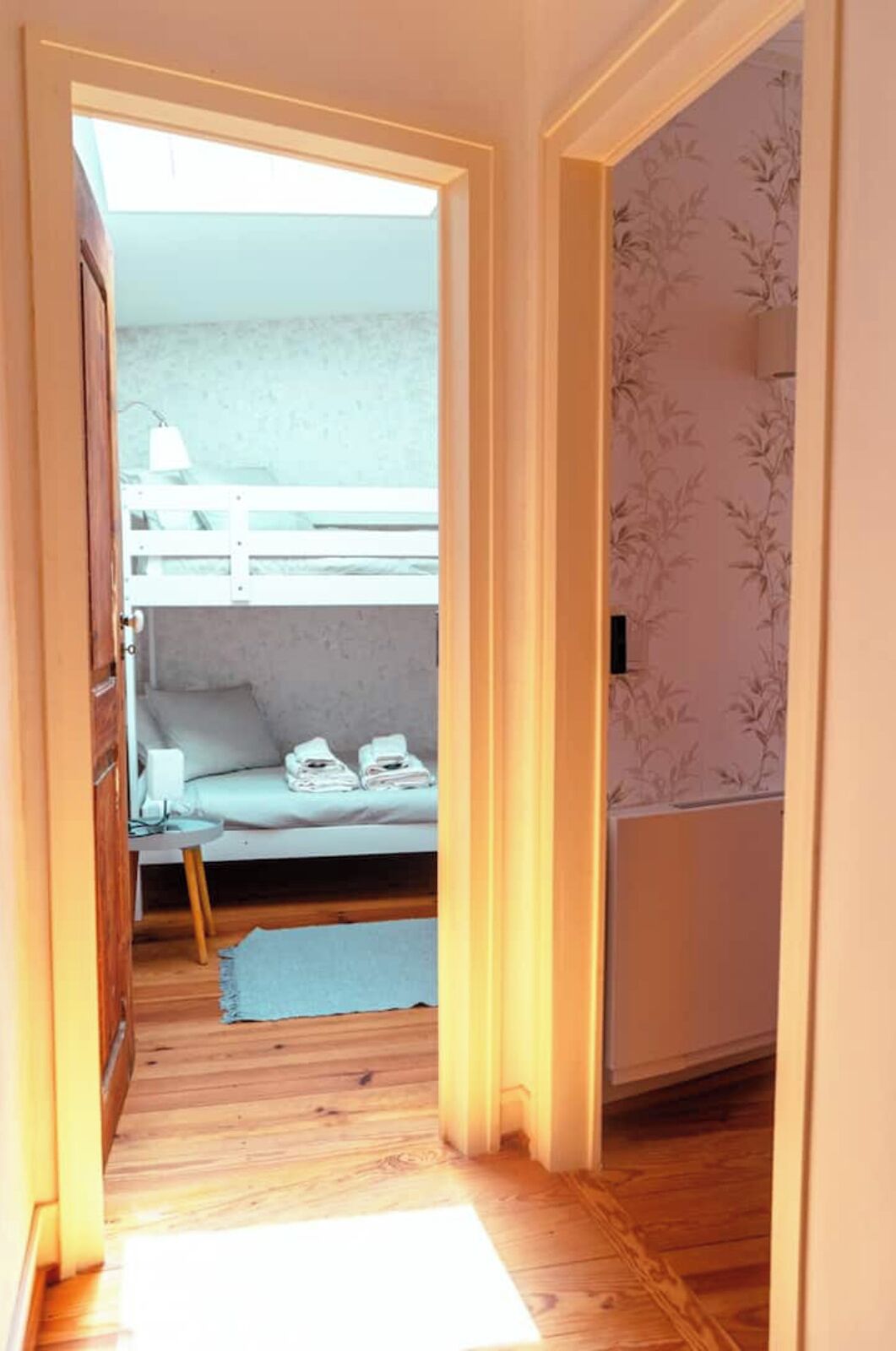 A narrow hallway leading to a room with a bunk bed, a small table with a lamp, and a radiator.