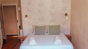 Una cama bien hecha con dos almohadas, una mesita de noche y una pared con estampado floral.