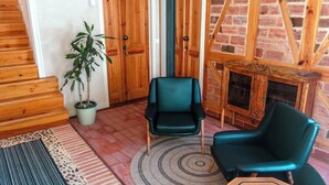 Una habitación con una escalera de madera, una planta en maceta, un sillón verde, un tapete estampado y una chimenea de ladrillo.