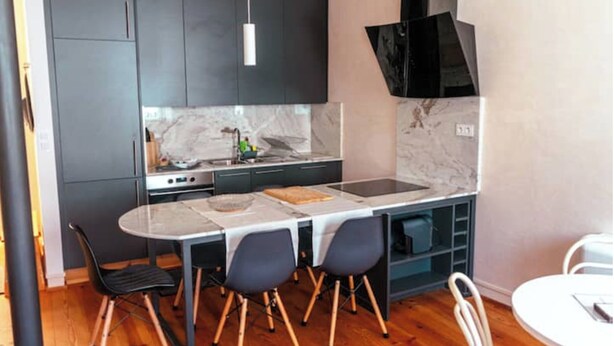 Cocina compacta con armarios oscuros, salpicadero de mármol, una isla central con taburetes e iluminación colgante moderna.