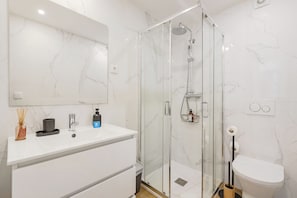 A modern bathroom with a glass-enclosed shower, a white vanity with a mirror, and a toilet.