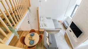 Un espace de vie compact comprenant un coin repas, un canapé, un téléviseur fixé au mur et un escalier avec une rampe en bois.