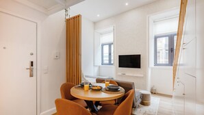 Un espace repas moderne avec une table ronde, des chaises orange et un téléviseur fixé au mur.